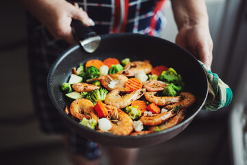 Woman cooking vegetables and shrimps on pan