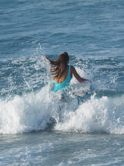 Back view of a surf woman with long hair in ocean. Female holding surfboard in wave. Active...