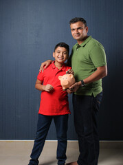 Father's day or finance education concept - Indian father teaching importance of saving to his son at home with piggy bank