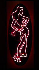 Neon sign full size naked woman in heels showing entrance to night strip dance club bar in red district of urban city adult entertainment.