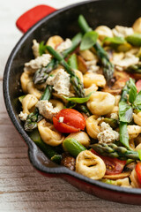 Cast iron pan with vegetable tortellini with asparagus, tomatoes, mushrooms and home made vegan feta cheese