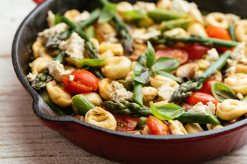 Cast iron pan with vegetable tortellini with asparagus, tomatoes, mushrooms and home made vegan feta cheese