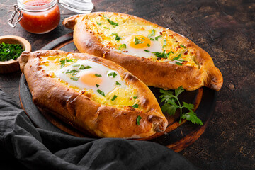  A traditional dish of Georgian cuisine, Adjarian khachapuri with cheese and egg and spicy tomato sauce adjika on the dark background close up
