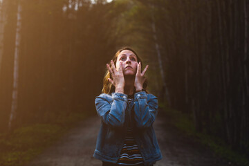 Portrait of a sad young woman wiping her face with her hands, looking at the sky. Melancholy girl walking alone in the forest, feeling lonely. Lifestyle and people concept.