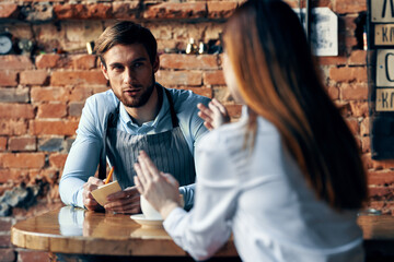 a man with a cup of coffee and all aprons at a cafe table and a woman in a shirt and red skirt cropped view