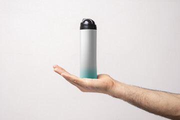 Male arm holding a bottle of shaving foam in front of gray background,