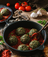 Vegan spinach balls with chickpeas in pan with tomato sauce, onion, parsley on dark background with...