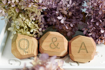 Letters Q and A written on wooden irregular blocks among flowers. Question and answer concept.....