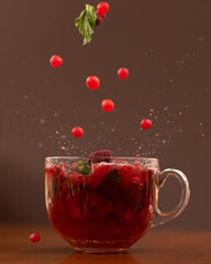 Mint leaves falling into glass cup with citrus herbal tea. Close up shot in motion on brown background, soft focus. Side view.
