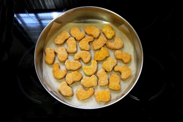 Frozen chicken nuggets ready to bake on baking paper on a baking tray on the kitchen counter. Selective focus from the top.