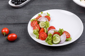 Fresh delicious salad with vegetables: tomato, cucumber, onions and greens with olive oil