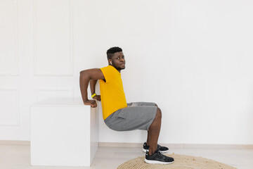 Full length view young handsome strong fit Afro American male in yellow sportswear deeply squatting...