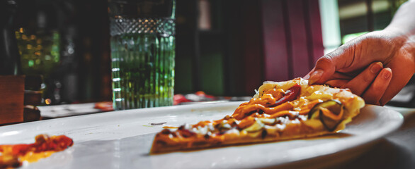 woman Hand takes a slice of meat Pizza with Mozzarella cheese, salami, Tomatoes, pepper, ham in cafe