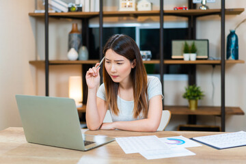 Concentrated Asian woman making decision or lack of idea working at home. Female trying to solve problems working from home while coronavirus pandemic