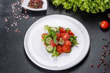 Fresh delicious salad with vegetables: tomato, cucumber, onions and greens with olive oil