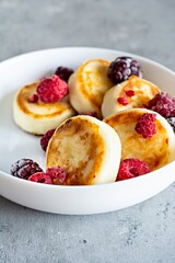 Fresh cottage cheese or ricotta  pancakes (syrniki,fritters) on a white plate with fresh berries on a blue background. Delicious healthy breakfast.  Ukrainian, Russian cuisine sweet food.