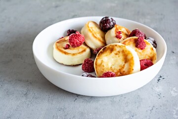 Fresh cottage cheese or ricotta  pancakes (syrniki,fritters) on a white plate with fresh berries on a blue background. Delicious healthy breakfast.  Ukrainian, Russian cuisine sweet food.