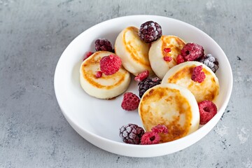 Fresh cottage cheese or ricotta  pancakes (syrniki,fritters) on a white plate with fresh berries on a blue background. Delicious healthy breakfast.  Ukrainian, Russian cuisine sweet food.