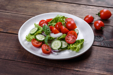 Fresh delicious salad with vegetables: tomato, cucumber, onions and greens with olive oil