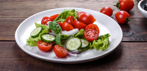 Fresh delicious salad with vegetables: tomato, cucumber, onions and greens with olive oil