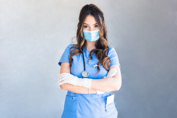 Confident young woman doctor standing with crossed arms wearing a protective mask and gloves.