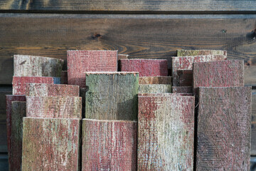 Several old planks are propped up against a new brown wooden wall. The sawn ends and the old partially peeling paint are visible. Background. Texture.