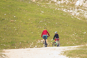 Mother and daughter cycling uphill with mountain bikes at a sunset.