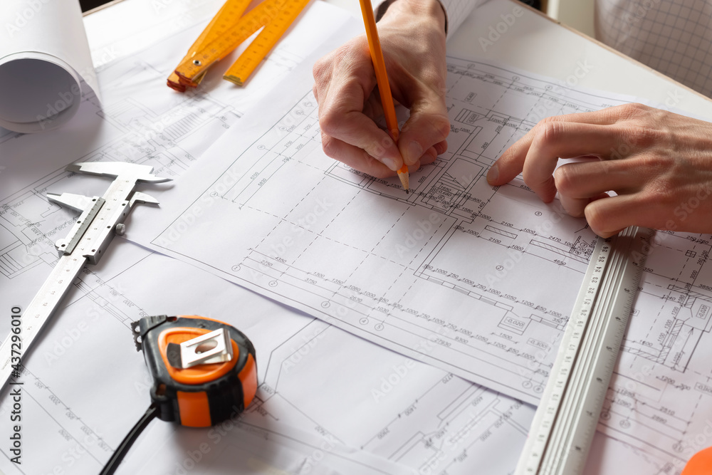 Poster the hands of the architect draw sketches and blueprints on the desktop.