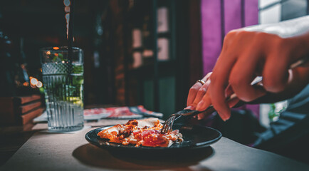 woman hands with knife and fork cutting pizza on table in cafe