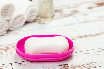 Fototapeta na wymiar soap on pink plastic soap dish with towels on white wooden table in bathroom