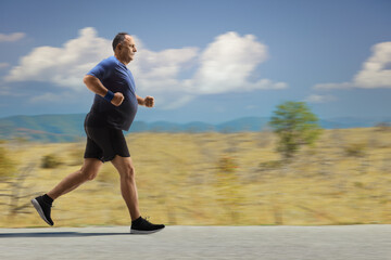 Corpulent mature man in sportswear jogging on an open asphalt road