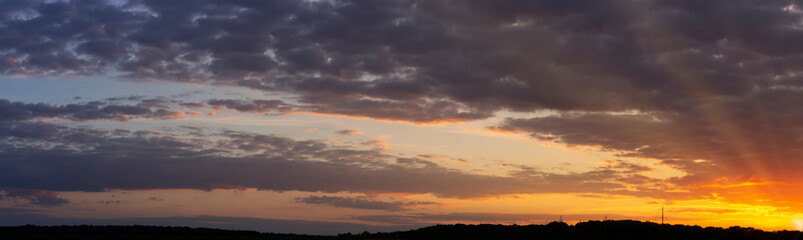 Fototapeta na wymiar Panorama of a beautiful sunset with purple clouds and sunbeams to the horizon.