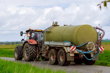 Poster Water tank for tractor trailer. Modern tractor with a cistern tank, on an asphalt road near agricultural fields. © Yaroslav