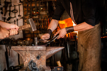 blacksmith with striker forges a horseshoe on the anvil with forging chisel, close-up blacksmith trains an assistant to work in a Forge on an anvil