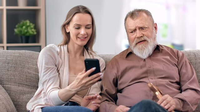 Happy young adult daughter granddaughter and 80s father grandfather studying use smartphone