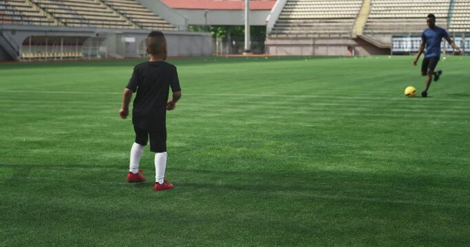 Black father kicking football ball to son