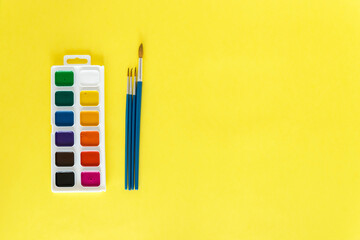 Paints and brushes on a yellow background.Back to school. The concept of education. Everything for school and office. School supplies. The child will draw Flatly. From above.
