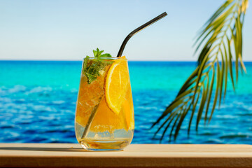 Summer alcohol drinks, beach cocktail party. Glass of gin tonic tropic cocktail with orange fruit and mint, blue sea on background. Summer resort concept.