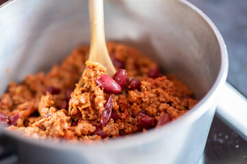 Close up and selective focus of a meat chilli concarne cooking on the hob in a stainless steel saucepan with shallow depth of field and bokeh