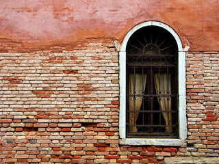 Fototapeta na wymiar Welcome to Venice - A red coloured brick wall of an old building with a rounded window in Venice, Italy.