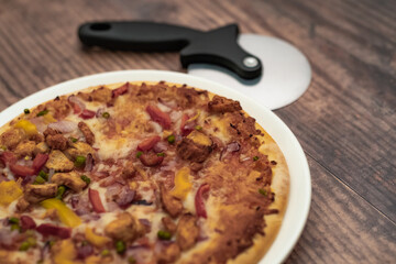 Close up and selective focus of a home cooked thin crust sweet chilli chicken pizza on a white plate on a wooden table