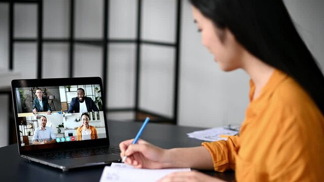 Video call, online conference using app and laptop. Satisfied asian female student or freelancer, studies or works remotely, watches an online lecture, takes notes, multiracial people on laptop screen