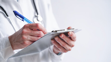 Close-up of a doctor writing a prescription in a medical record on a tablet. A doctor in a white coat writes a prescription with a blue pen. Medical banner concept, copy space