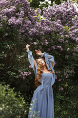 Woman in long dress next to lilac in garden in summer for a walk