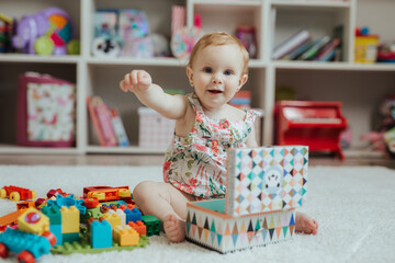 Little curious baby girl playing on a playground in a bright sunny room. Learning and playing colorful educational blocks game and puzzle