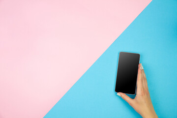 Young woman hand holding smartphone with black screen on light pink blue table background. Copy space empty place for text inscription. Mobile application interface concept design. Modern technology.