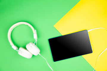 Set of business, designer or educational gadgets and accessories from top view. White headphones, tablet with blank screen are lying on yellow mint background. Copy space for advertising text.