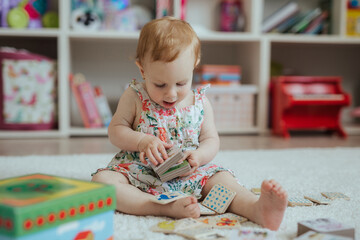 Little curious baby girl playing on a playground in a bright sunny room. Learning and playing colorful educational blocks game and puzzle