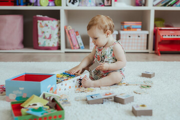 Little curious baby girl playing on a playground in a bright sunny room. Learning and playing colorful educational blocks game and puzzle