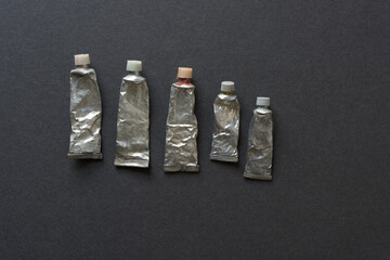 old dried out watercolour paint tubes individually arranged on a dark grey board